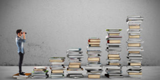 Junger Mann mit Fernglas vor Bücherstapeln