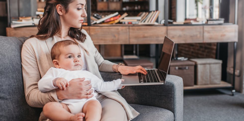 Frau mit Kind auf dem Arm und Laptop neben sich