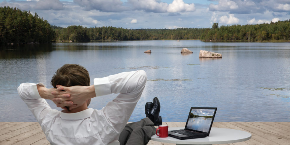 Mann im Anzug sitzt mit Beinen auf dem Tisch an einem See