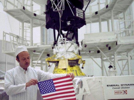 Grüße in 60 Sprachen, verewigt auf einer goldenen Datenplatte, sowie natürlich die amerikanische Flagge gehörten zu Erstausstattung von Voyager, die Projektleiter John Casani 1977 stolz präsentierte. Im Hintergrund: Voyager 2.