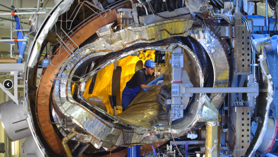 Ende 2011 war das Innenleben von Wendelstein 7-X noch sichtbar. Jetzt ist die ringförmige Anlage geschlossen. Vom Zentrum nach außen: das Plasmagefäß, eine der verwundenen Stellaratorspulen (silberfarben), eine ebene Spule (kupferfarben), die Stützstruktur (rechts) und das Außengefäß zusammen mit zahlreichen Kühlleitungen und Stromverteilern.