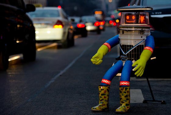 "Nehmt mich mit": Roboter hitchBOT sitzt am 12. Februar 2015 in München am Straßenrand – und lächelt in die Kamera. Denn so allein, wie´s aussieht, ist er nicht. Seit seiner Reise durch Kanada ist er ein Medienliebling. Was seine Fans aber zunehmend stört.