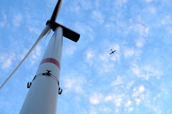 Ein Flugzeug über dem Windpark Langenhorn, der als erster Windpark Deutschlands mit dem System Airspex ausgestattet wurde. Eine Radarantenne ist am Turm der Windenergieanlage zu sehen.