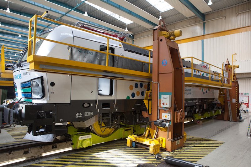 Die Vectron-Lok im Werk München-Allach: Auf ihrem Weg nach Finnland kamen beim Transport auf deutschen Normalspurgleisen erstmals neu entwickelte Hilfsfahrgestelle (Loco Buggy) zum Einsatz. Jeder der vier Radsätze des 90 Tonnen schweren Verton stand dabei auf einem Loco Buggy. Dieses Transportsystem wird erstmalig eingesetzt.