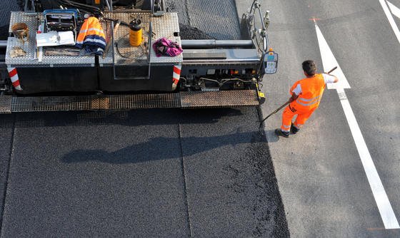 Straßenarbeiter bringen eine Asphaltdecke auf: Das Bitumen – also die klebrige Masse, in die der Splitt eingebettet ist – gewinnt man bislang aus Erdöl. Mikroalgen könnten eine ressourcenschonende Alternative sein. 