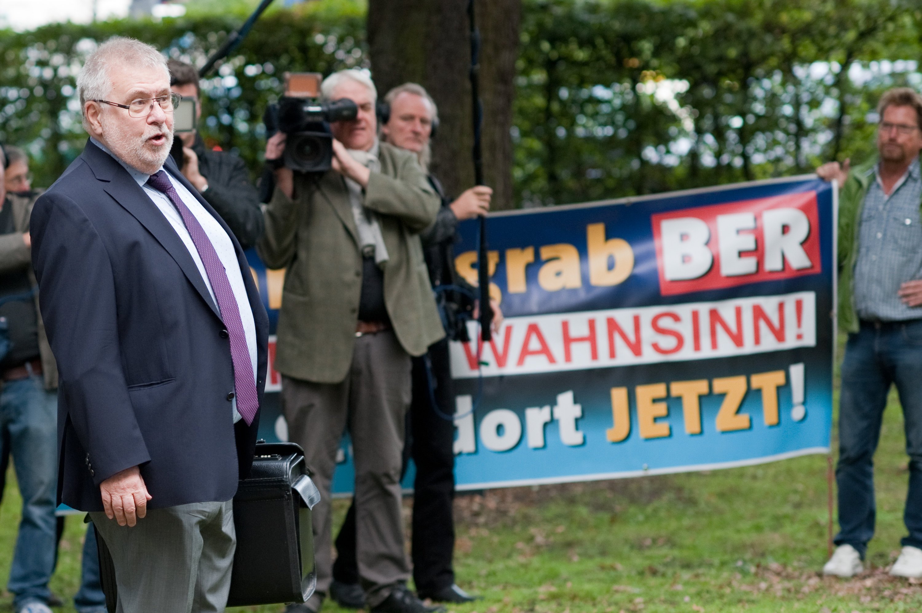 Der Brandenburger Flughafenkoordinator, Staatssekretär Rainer Bretschneider, am 25. September 2015 vor der Aufsichtsratssitzung der Flughafengesellschaft Berlin-Brandenburg: Demonstranten protestieren gegen das Milliardengrab BER. Jetzt rätseln auch Politiker, ob es noch Sinn macht, den Flughafen noch zu vollenden.