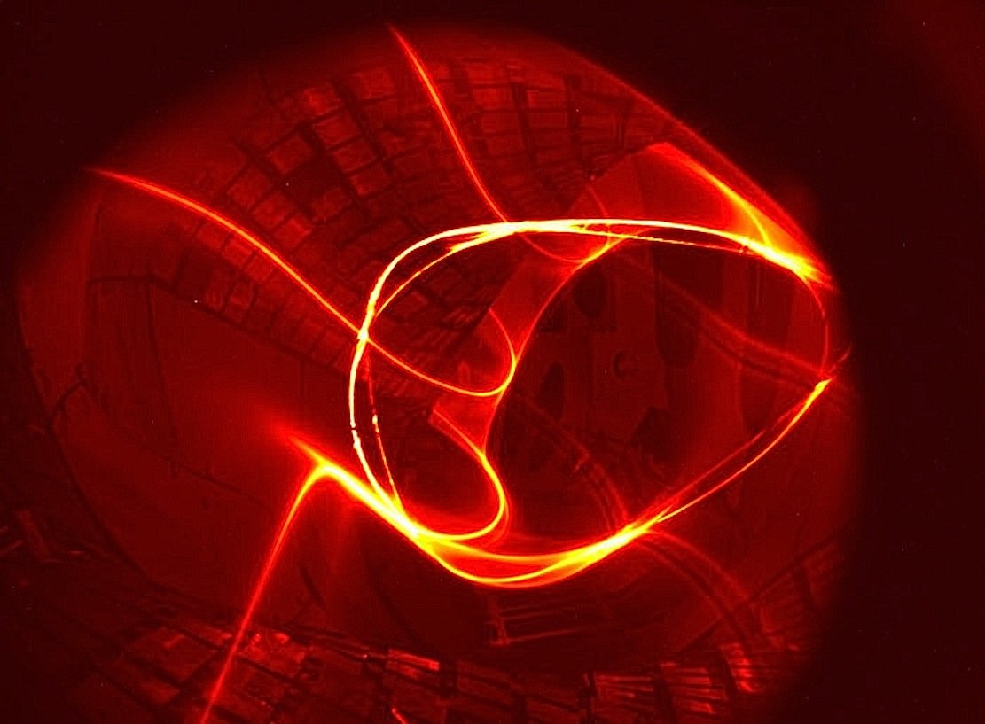 Das erste Magnetfeld im Fusionsreaktor Wendelstein 7-X wurde im Juli 2015 erzeugt. Das Foto kombiniert die Leuchtspur eines Elektronenstrahls auf seinem vielfachen Umlauf längs einer Feldlinie durch das Plasmagefäß mit den Bildpunkten, die er auf einem fluoreszierenden Stab hinterlässt, der durch die Bildebene geschwenkt wird. Der schnell bewegte Stab ist wegen der langen Belichtungszeit nicht zu sehen.