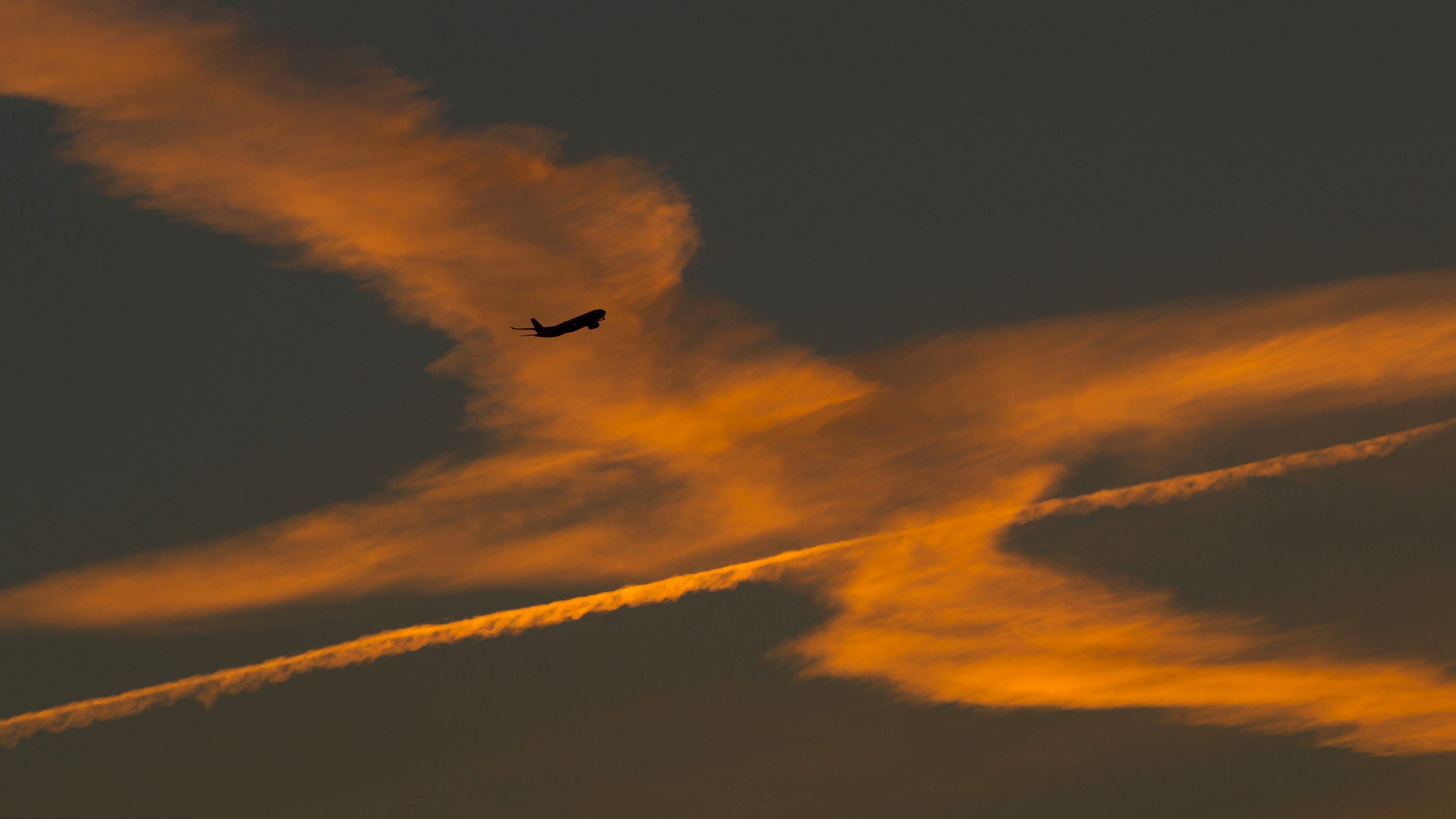 Ein Flugzeug im Anflug auf den Flughafen von Frankfurt am Main (Hessen) passiert Kondensstreifen von vorhergehenden Maschinen, die von der aufgehenden Sonne orange beleuchtet werden. 