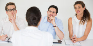 Drei Personen im Business-Kontext sitzen einer Frau gegenüber