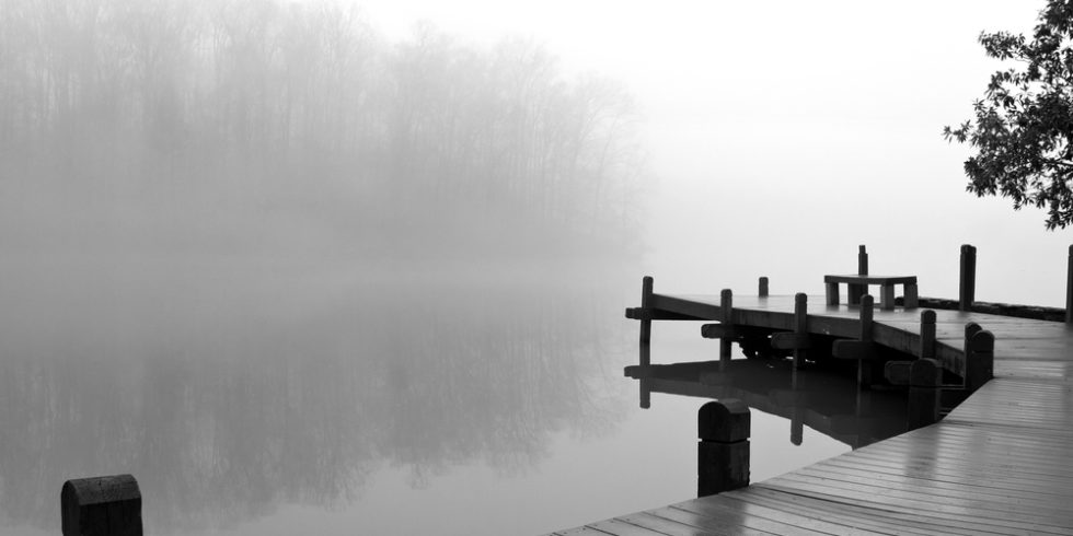 Schwarz-weiß Bild eines Stegs über nebligem Wasser