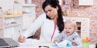 Frau mit kleinem Kind und Telefon am Ohr am Schreibtisch