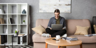 Mann mit Laptop auf dem Schoss auf dem Sofa