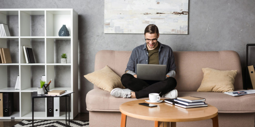 Mann mit Laptop auf dem Schoss auf dem Sofa