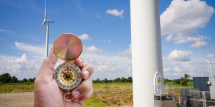 Männerhand hält Kompass vor einem Feld mit Windrädern