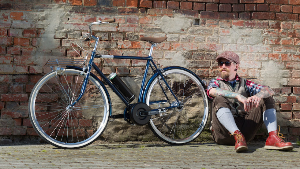 Mann sitzt neben seinem Bike vor einer Backsteinwand