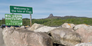 Schild "Welcome to Isle of Eigg" vor grüner Hügellandschaft