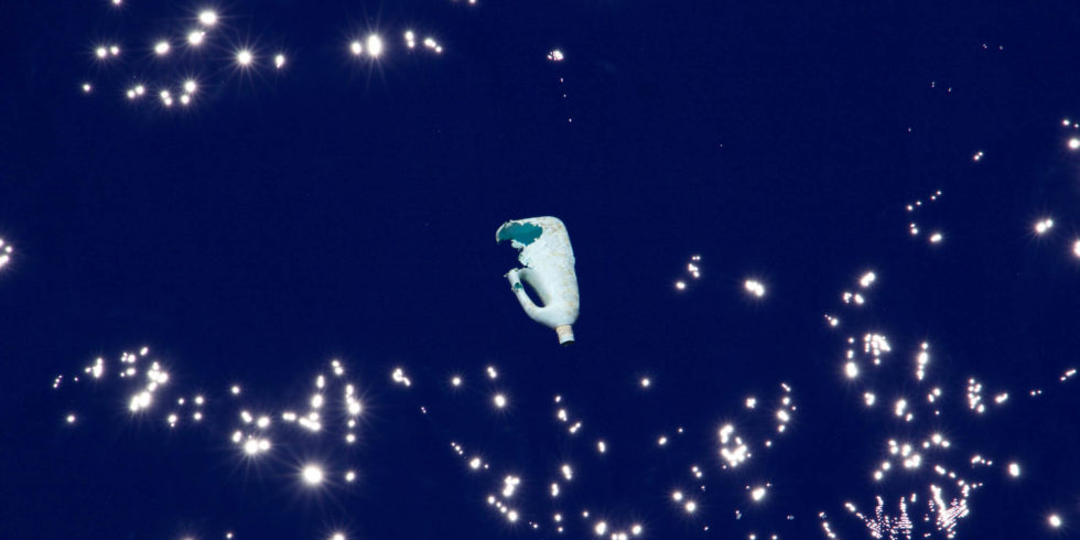 Man sieht eine weiße Plastikflasche, die im Meer treibt.