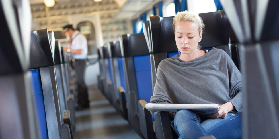 junge Frau sitzt in Zug, im Hintergrund sieht man einen Kontrolleur