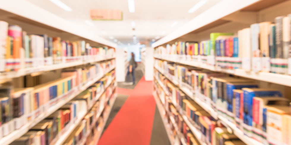 Blick in eine Bibliothek mit weißen Regalen rechts und links des Ganges