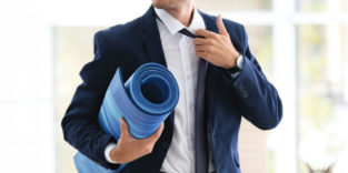 Mann im Anzug mit einer Yogamatte unter dem Arm steht symbolisch für betriebliches Gesundheitsmanagement