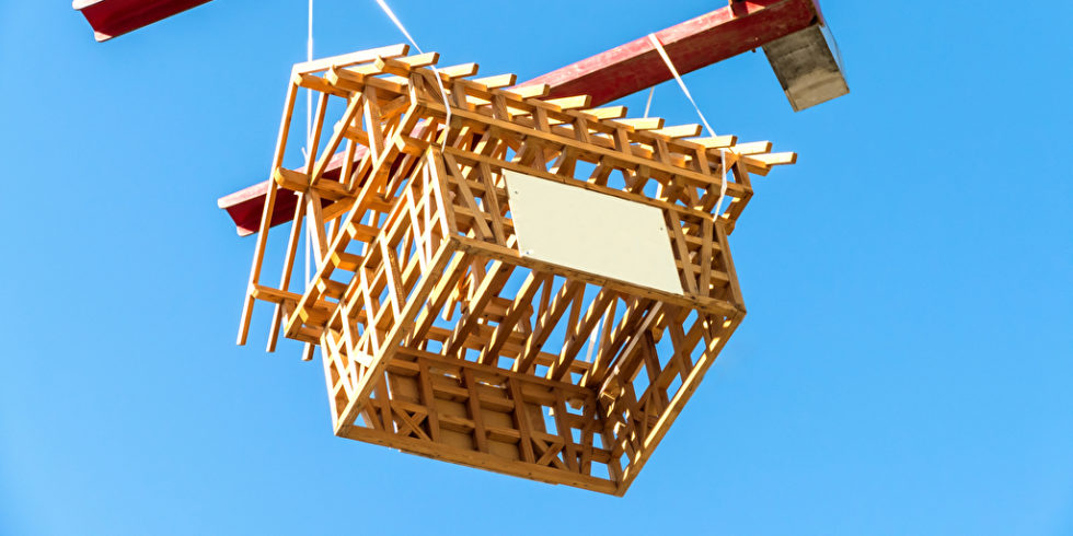 Holzhaus Grundstruktur hängt an einem Kran vor blauem Himmel