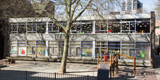 Gebäude mit vielen Bastelarbeiten in den Fenstern und Hof davor, vermutlich ein Kindergarten