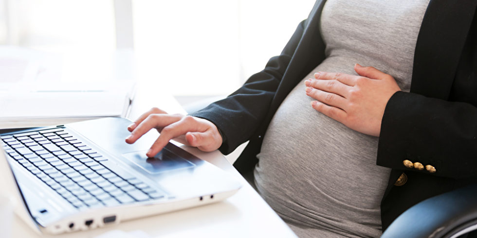 Schwangere Frau sitzt vor Laptop