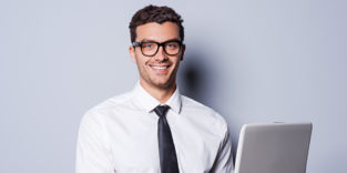 Mann im Hemd und Krawatte am Laptop arbeiten und lächelnd stehen vor grauem Hintergrund