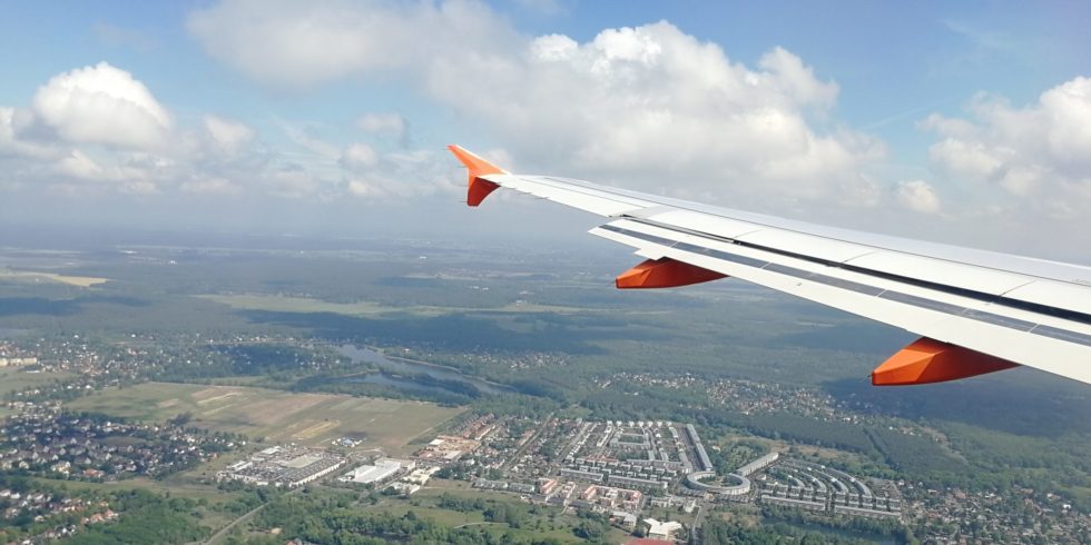 Blick aus dem Flugzeug auf die Tragfläche und eine Stadt von oben