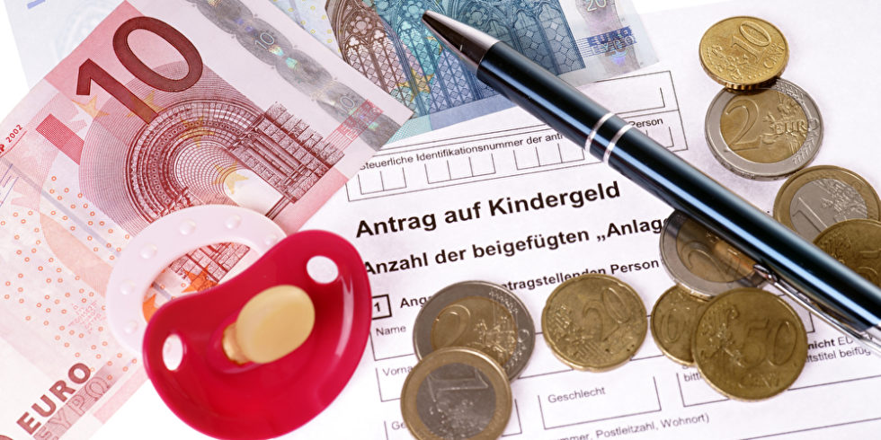 EUroscheine und Münzen sowie ein Schnuller liegen auf einem ausgedrucktem Antrag auf Kindergeld