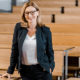 Frau in dunklem Anzug und Brille in einem Hörsaal