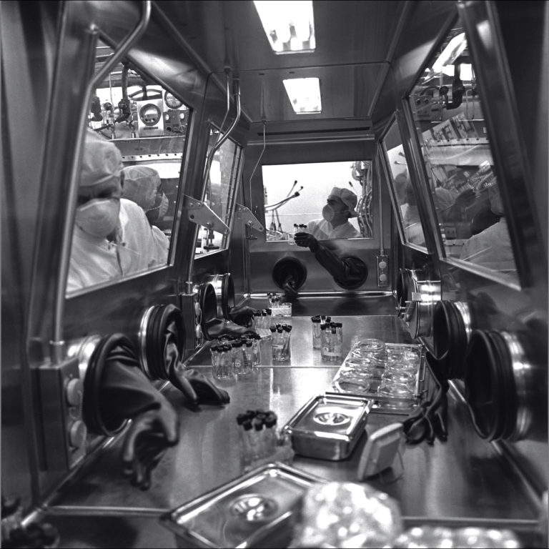 schwarz-weiß Bild von Wissenschaftlern, die Proben in einem Glaskasten untersuchen