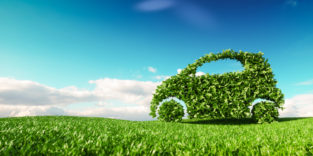 Grünes Auto aus Blättern auf Wiese vor blauem Himmel