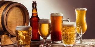 verschiedene gefüllte Biergläser stehen vor einem hölzernen Fass