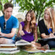 junge Menschen sitzen mit Laptop und Büchern im Park / Campus