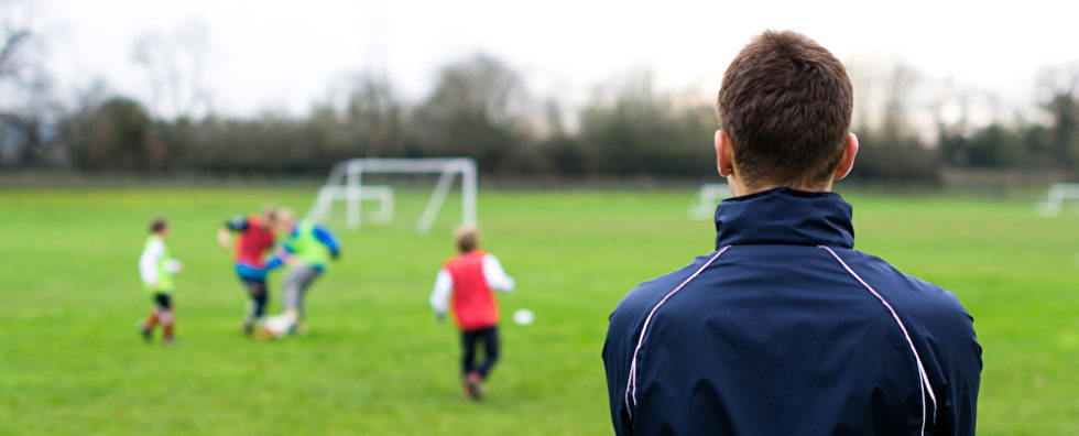 Mann schaut auf einen Fußballplatz, auf dem Kinder spielen