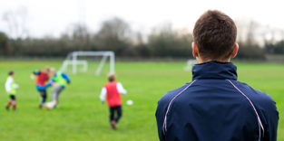 Mann schaut auf einen Fußballplatz, auf dem Kinder spielen