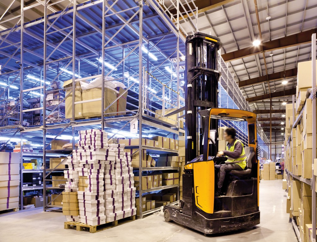 Worker in the motion on forklift in the large modern warehouse