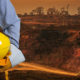 Ingenieur mit einem gelben Helm für die Sicherheit der Arbeiter auf dem Hintergrund der Kohlebergbau-Lkw fahren auf der Straße. Der Sonnenuntergang
