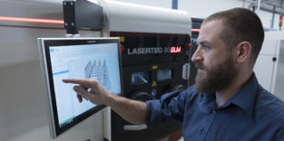 Mann bearbeitet CAD-Daten am Bildschirm eines 3D-Druckers