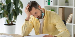 Mann mit Maske unterm Kinn blickt auf Blätter