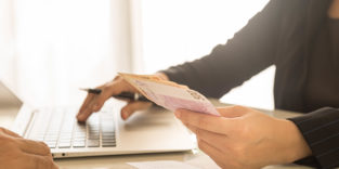 Mann überreicht Geldscheine Latop