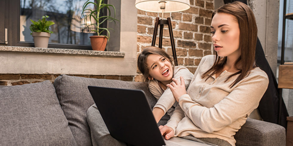 Frau mit Laptop auf Sofa und Kind im Hintergrund