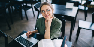 Frau sitzt vor Büchern und Laptop