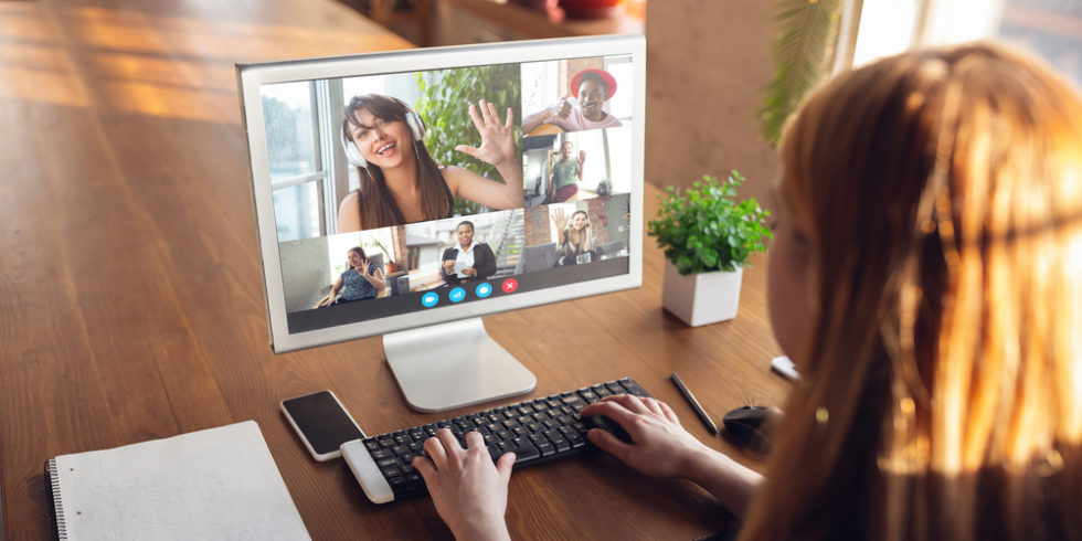 Frau im Homeoffice vor Monitor, auf dem virtuelle Konferenz zu sehen ist