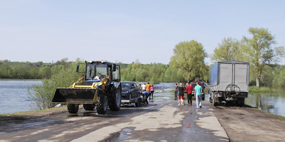 Nach dem Hochwasser sind viele Zufahrtsstraßen nicht mehr passierbar. Traktoren transportieren Autos durch das stehende Wasser.Foto: PantherMedia/Tsomkaigor