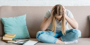 Junge Frau mit Händen im Kopf auf Sofa neben sich Bücher