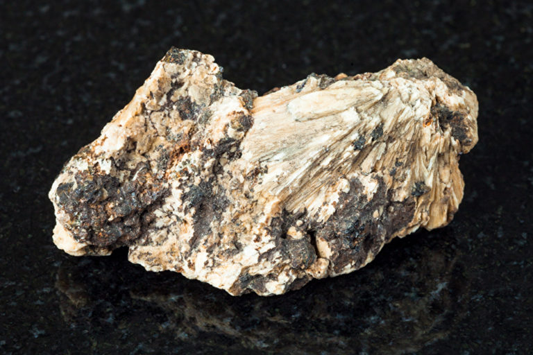 Makro-Schießen von natürlichen Mineral - schwarze Kristalle aus Perowskit-Stein in rohen Clinochlore Felsen auf schwarzem Granit aus Ural-Gebirge
