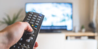 Mensch hält Fernbedienung vor TV-Gerät