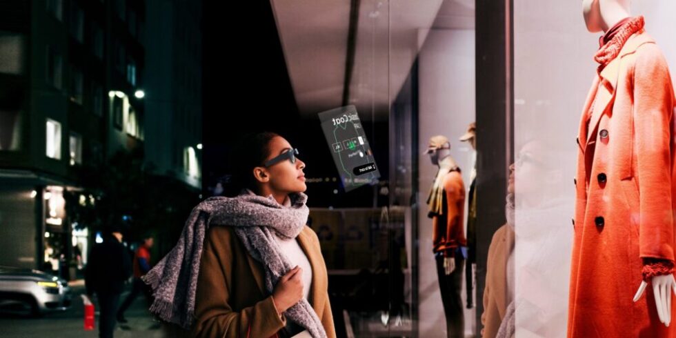 Frau mit AR-Brille steht vor einem Schaufenster eines Modegeschäfts